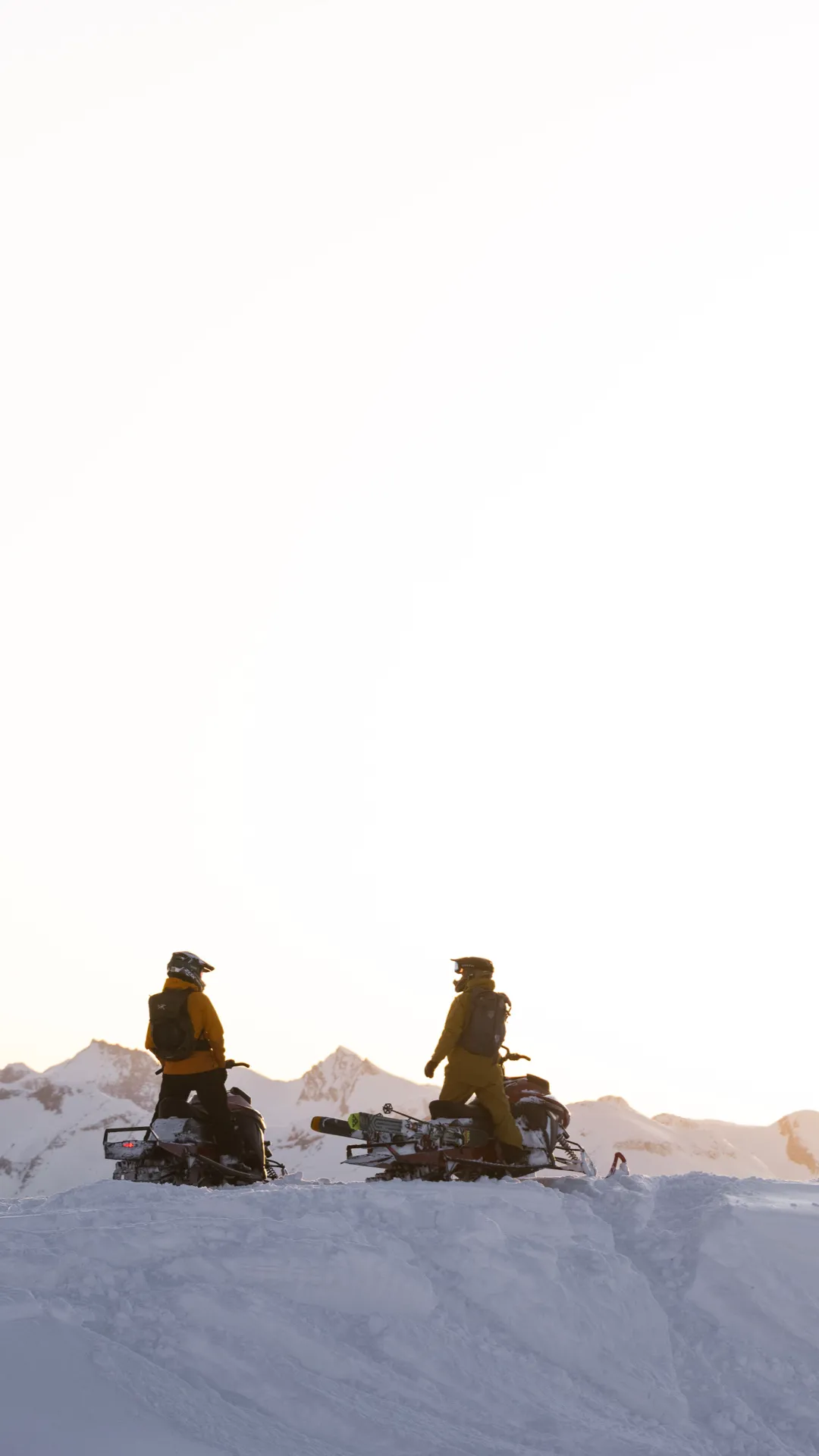 two people sitting on their sleds looking at the sun set